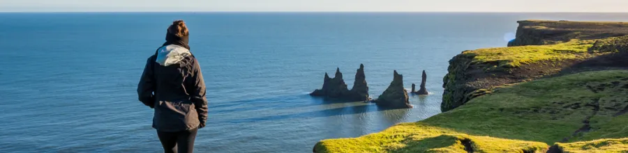 En person på Dyrhólaey med utsikt over Reynisdrangar og Atlanterhavet.