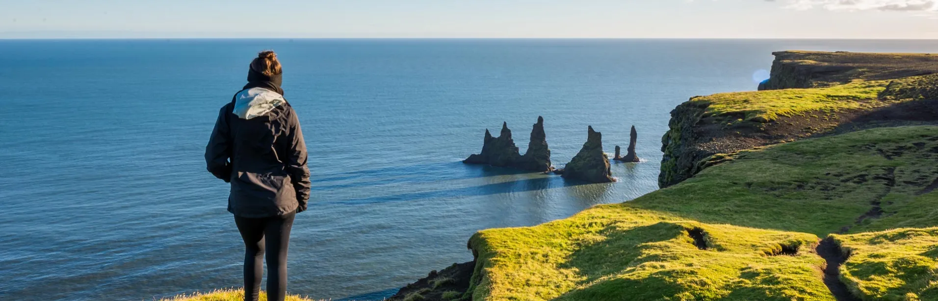 En person på Dyrhólaey med utsikt over Reynisdrangar og Atlanterhavet.