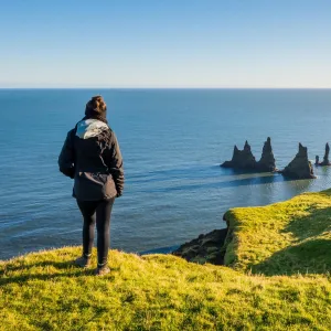 En person på Dyrhólaey med utsikt over Reynisdrangar og Atlanterhavet.